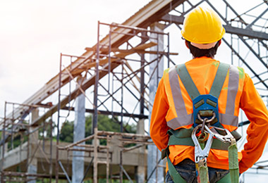 Construction worker wearing hard hat and fall protection harness next to a scaffold