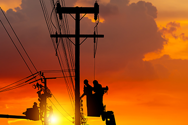 Silhouette of workers working on power lines with a sunset in the background