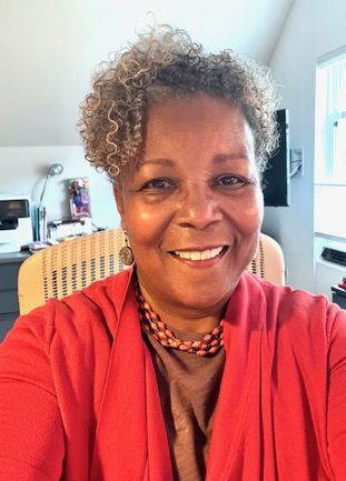 New Board Chair Carmen Sneed smiles in red outfit in her home office